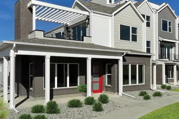 Modern townhouse exterior with a red door, brick facade, and flat rooftop patio under a pergola structure
