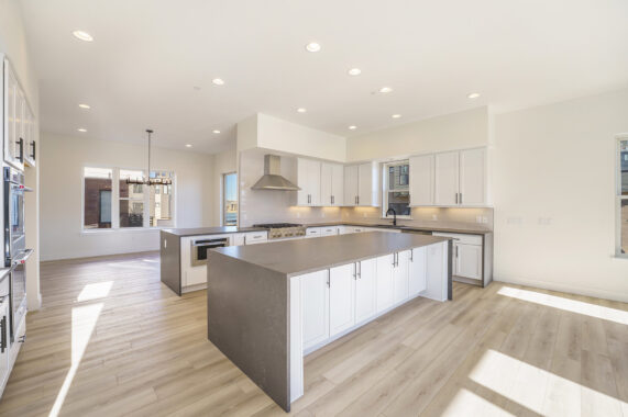 Modern kitchen with white cabinets, stainless steel appliances, gray countertops, and light wood flooring